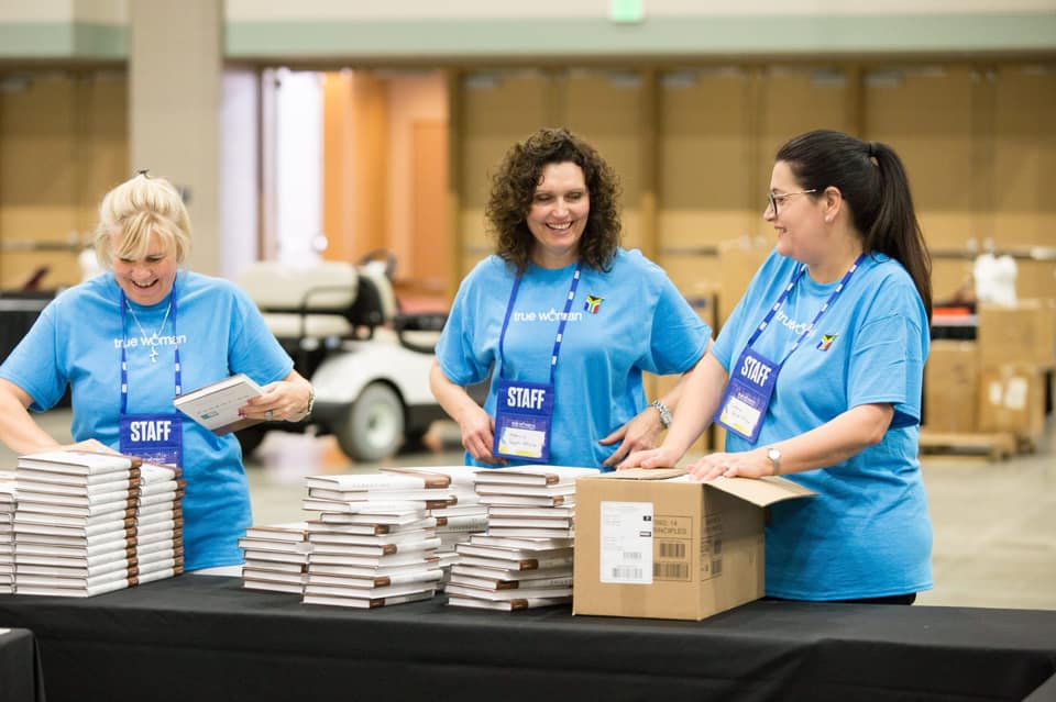 Three Revive Our Hearts event staff in blue True Woman shirts unpacking books at a conference